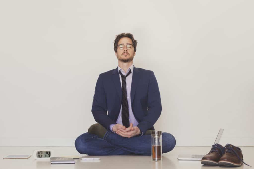 A handsome man wearing a suit and a tie meditating on the floor